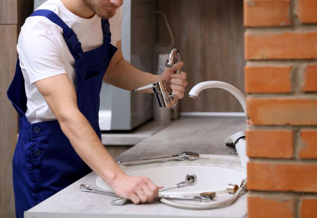 Plumber installing a new faucet in a kitchen sink, showcasing HD Drain Cleaning’s faucet installation services in Ormond Beach, FL